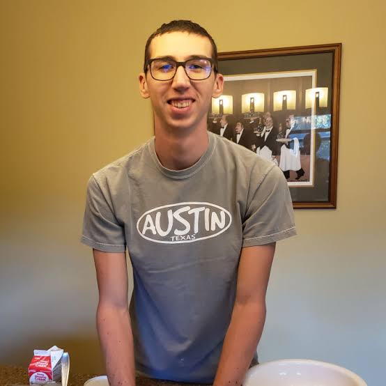 Alex smiling in a kitchen while wearing an Austin T-shirt