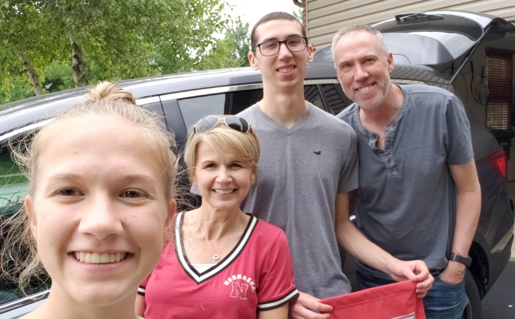 Alex and his family smiling together beside a vehicle
