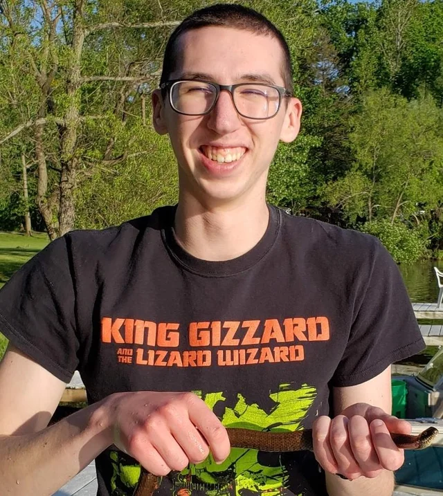 Alex smiling outdoors in a black band T-shirt